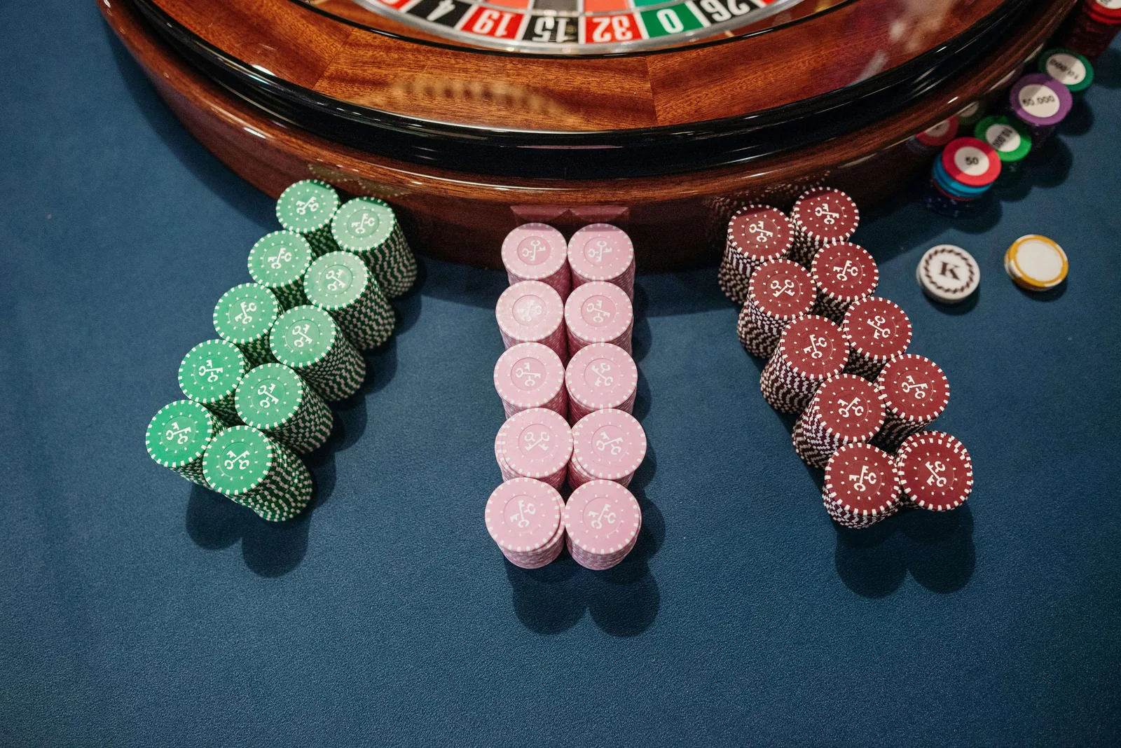 Casino chips arranged on a navy Velvetine layout beside a roulette wheel