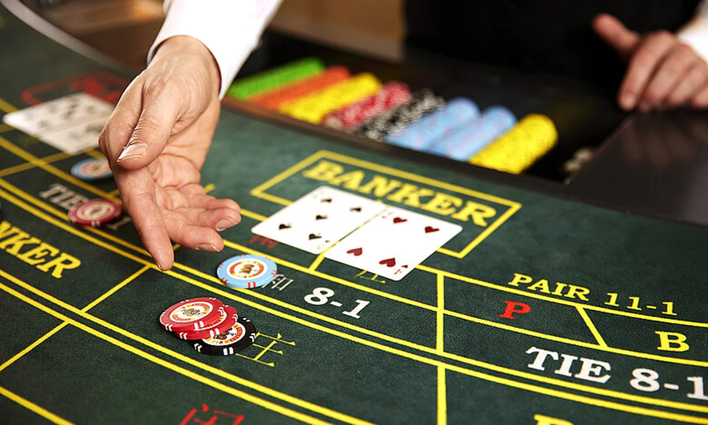 A green Baccarat layout with a dealer placing cards in the Banker box, chips and side bets visible