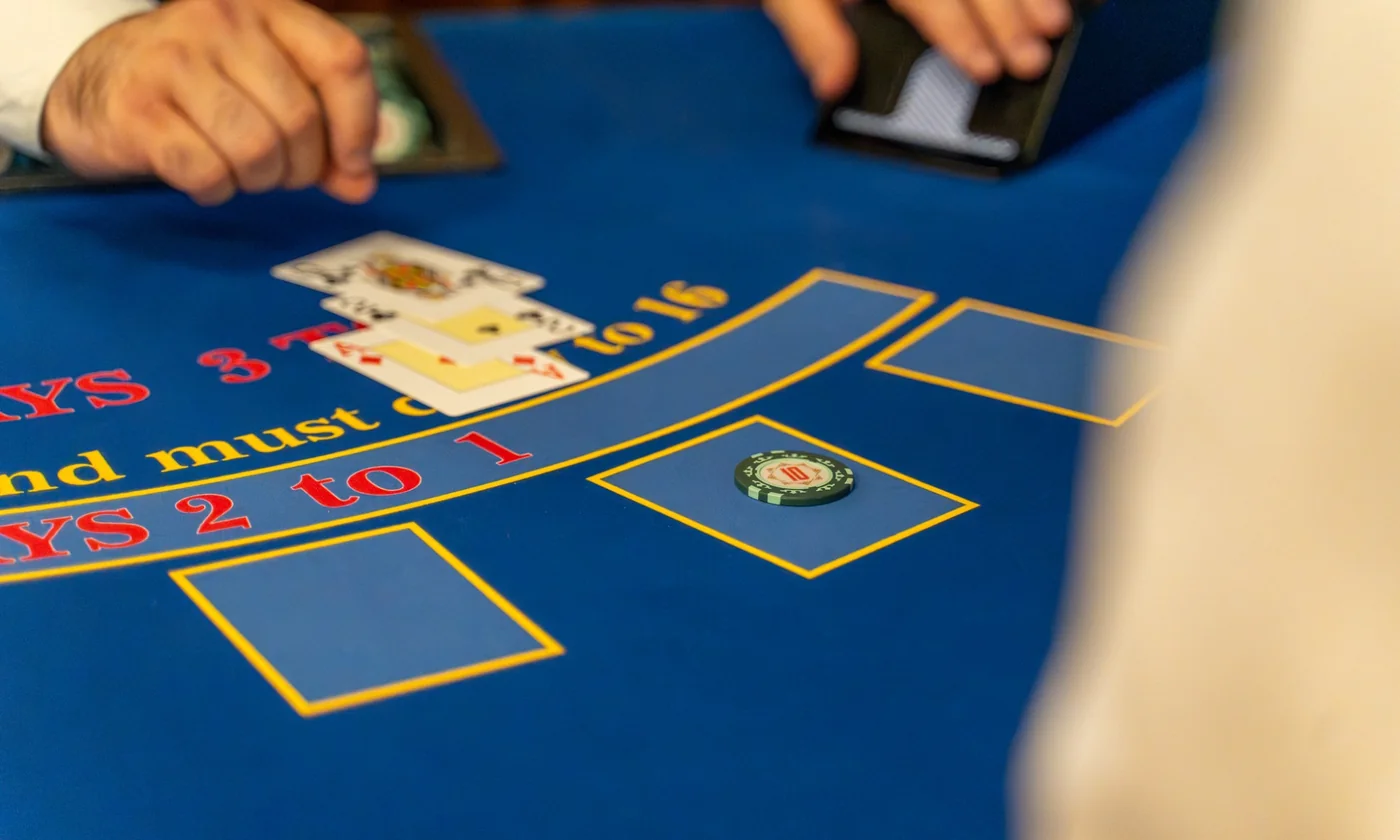 A dealer mid-play at a blue Blackjack layout, cards on the felt and a chip on the middle box